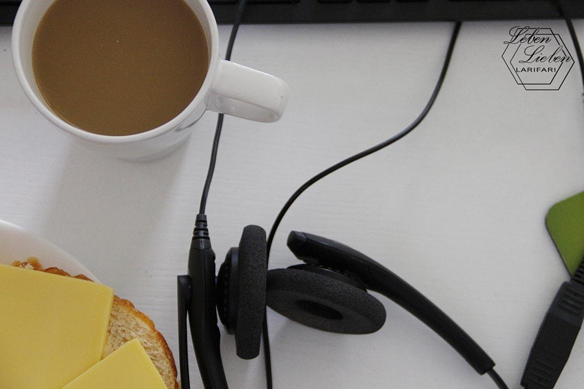 Zu sehen ist eine gefüllte Kaffeetasse, ein Headset und ein Ausschnitt eines Käsebrots - alles von oben