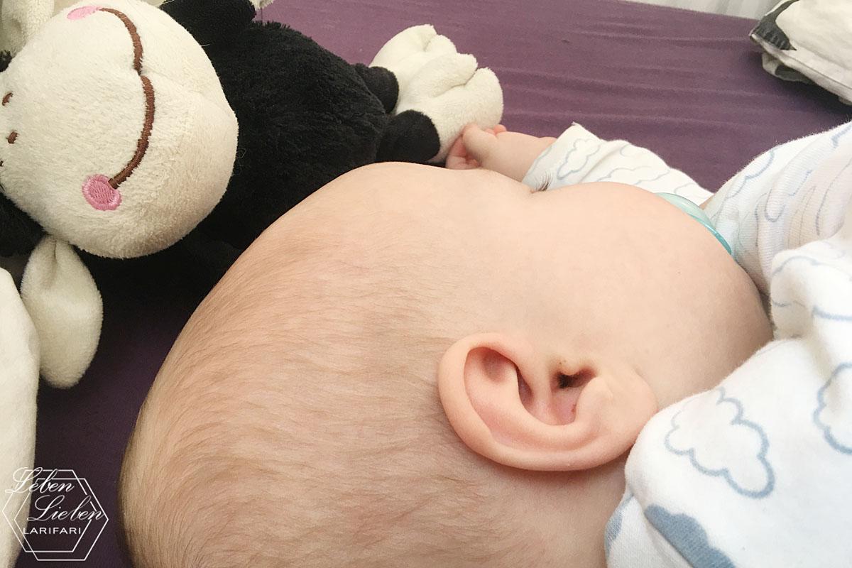 Ein Baby schläft an ein Kuscheltier-Schaf gekuschelt
