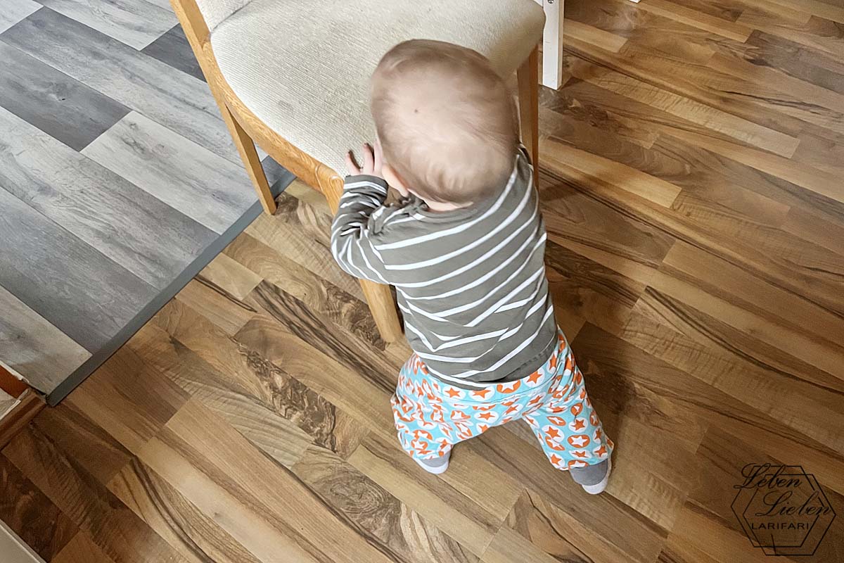 Ein Baby steht an einem Stuhl zwischen zwei Räumen