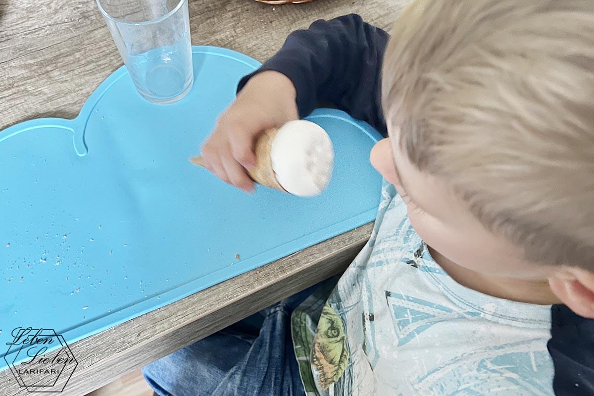 Kind sitzt am Tisch und isst ein Eis