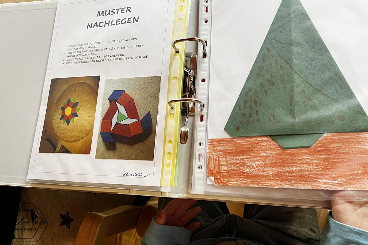 Ein Ordner, in dem Montessori-Arbeiten abgeheftet sind. Links zu sehen sind nachgelegte Muster, rechts ein gefalteter Tannenbaum