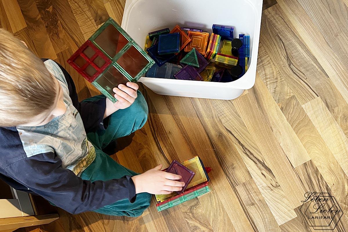 Ein Kind sitzt auf dem Boden, hat eine Kiste voller Magnetbausteine neben sich und baut mit selbigen