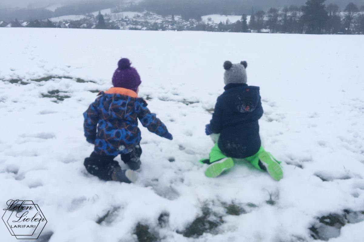 2 Kinder sitzen im Schnee und wollen einen Schneemann bauen