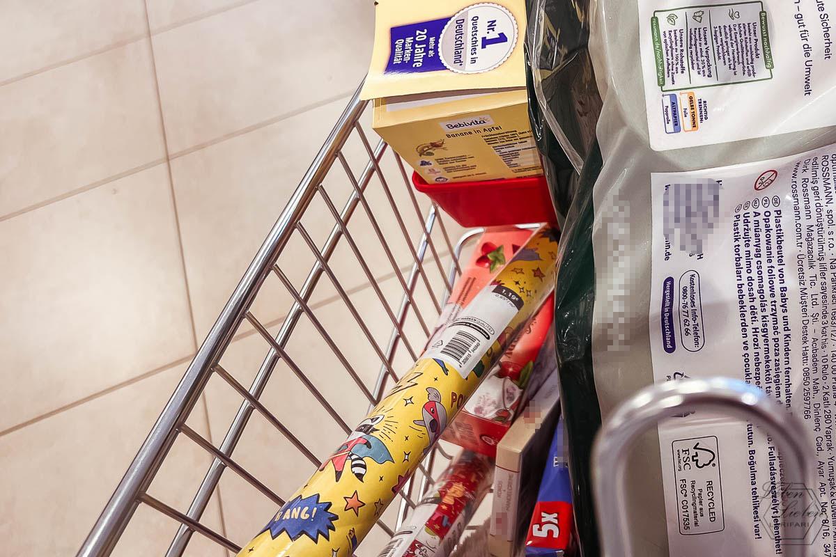 Ein Einkaufswagen mit Geschenkpapier, Obst-Quetschies und Toilettenpapier