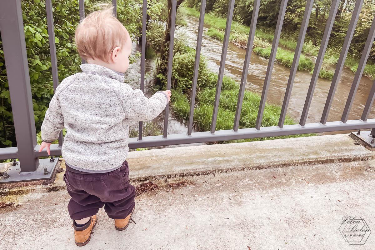 Ein Kleinkind steht auf einer Brücke und schaut runter aufs Wasser