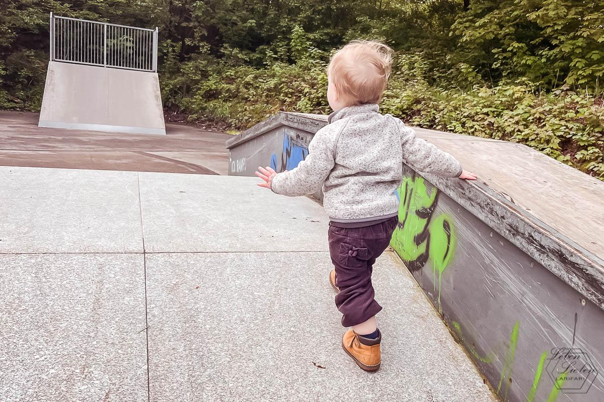 Ein Kleinkind läuft eine Skaterampe hoch, im Hintergrund ist eine höhere Rampe zu sehen