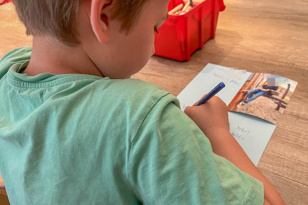 Ein Kind schreibt, im Hintergrund eine Box mit Stiften